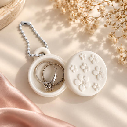 Close-up of an open white floral ring holder keychain showing the small jewelry compartment, raised flower design, and coordinating white ball chain.