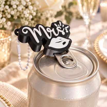 Mrs can tab opener fitted over a beverage can pull tab, with its white ball chain visible against a wedding table setting.