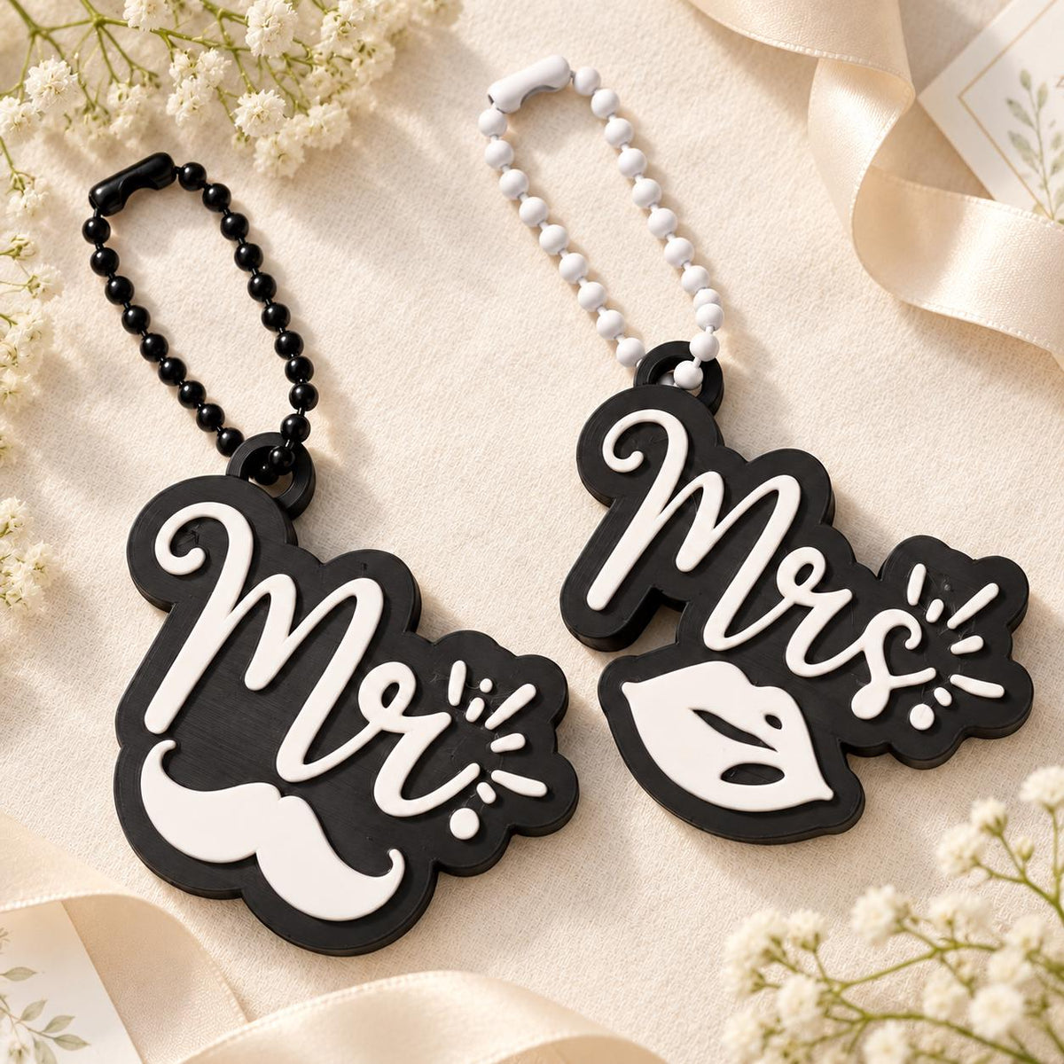 Black and white Mr and Mrs can opener keychains with mustache and lips designs, matching ball chains, and ivory wedding decorations.