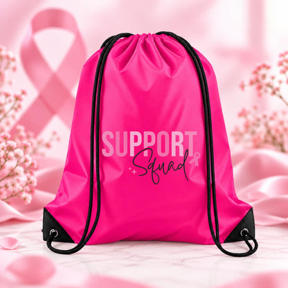 Bright fuchsia pink drawstring backpack featuring Support Squad breast cancer awareness typography with a small pink ribbon and black script lettering.